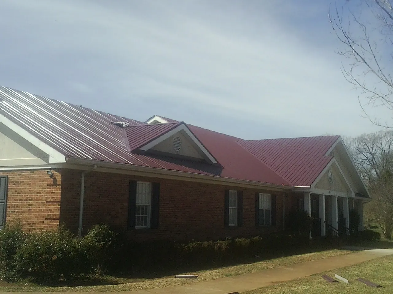 Red metal roof with gabled entries on a long brick building, from a Hail Damage Roof Repair job in Pontotoc