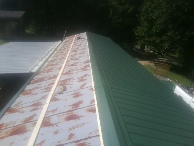 Old rusted panels beside newly installed green metal roofing — Wind Damage Roof Repair by Roofing Brothers in Pontotoc