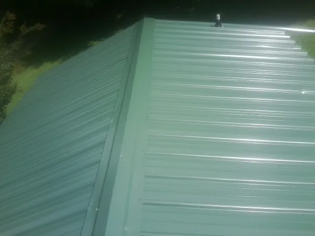 New green metal panels meeting at the ridge of a roof — Flat Roof Repair work by our crew in Pontotoc