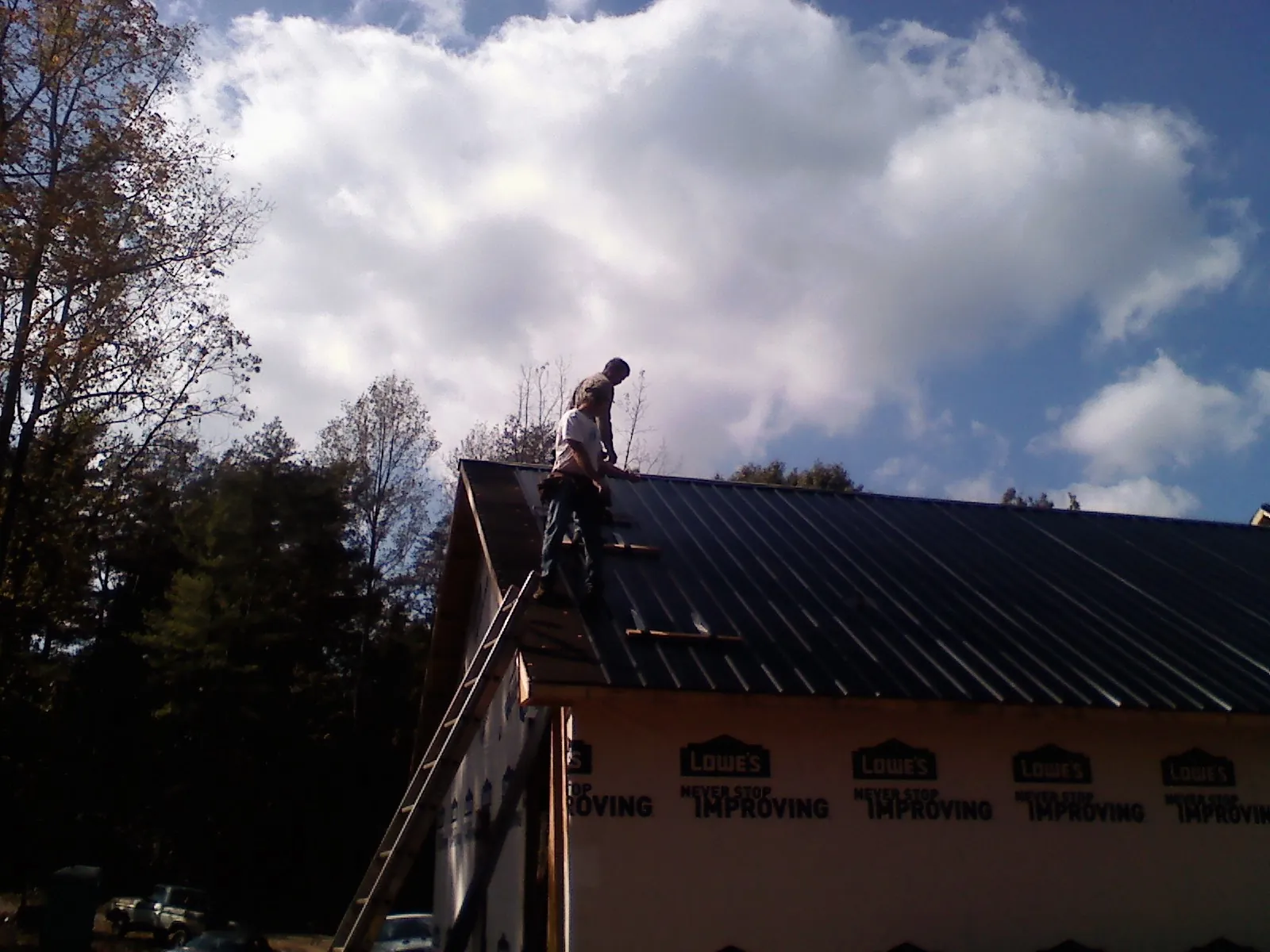 Roofer fastening dark metal panels high against a cloudy sky, from a Roof Inspection job in Pontotoc