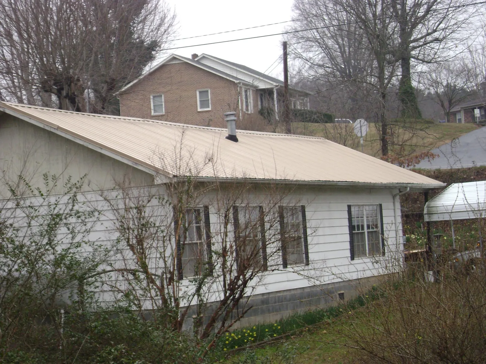 Tan metal roof on a white sided house set into a hillside — Commercial Roofing by Roofing Brothers in Pontotoc