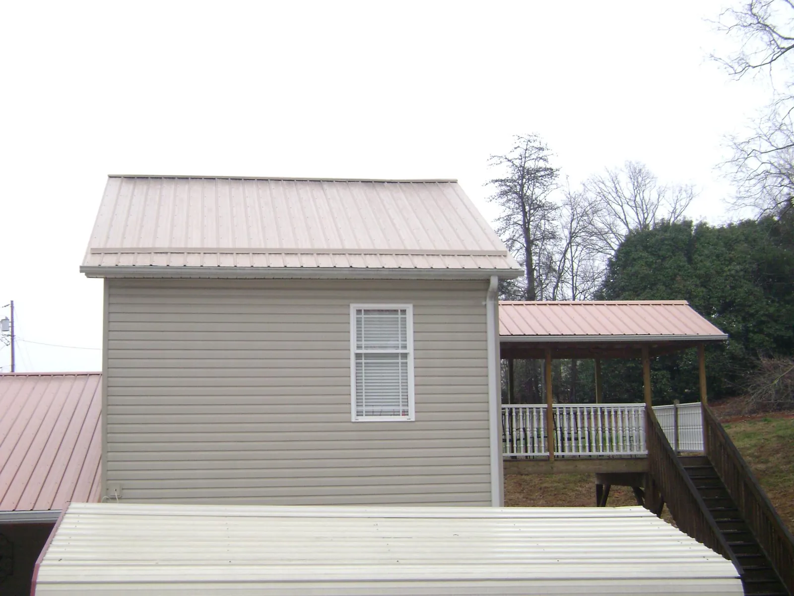 Tan metal roofs on a two story addition and attached porch, from a Roof Replacement job in Pontotoc
